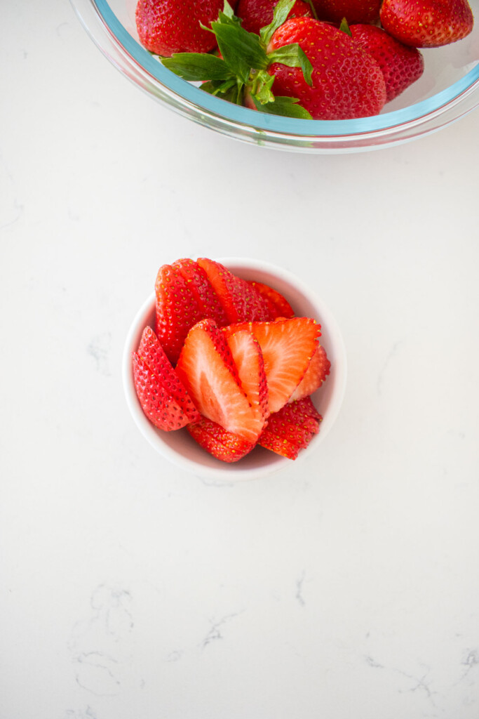 sliced strawberries in a small bowl on a white marble counter.
