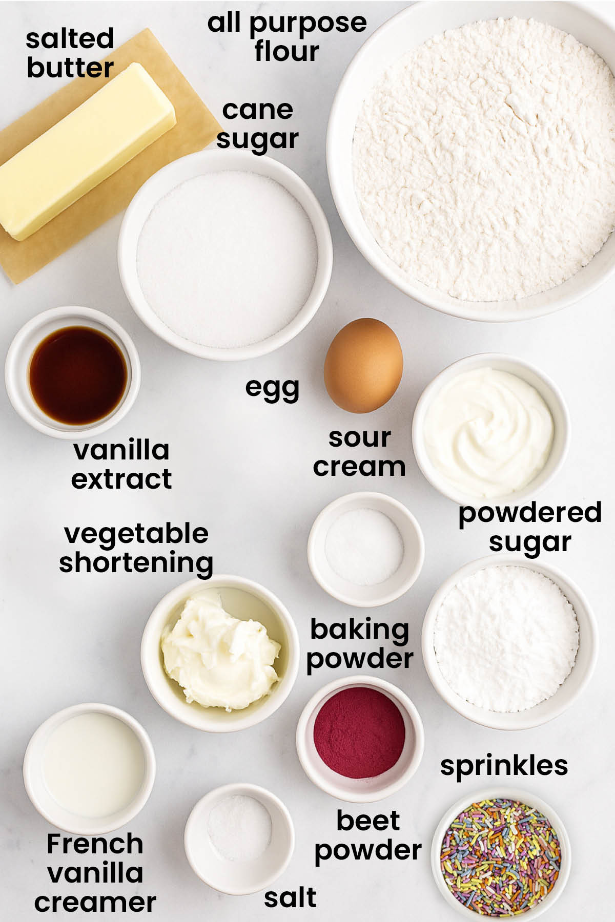individual ingredients for soft sugar cookies with pink frositng laid out against a white background.
