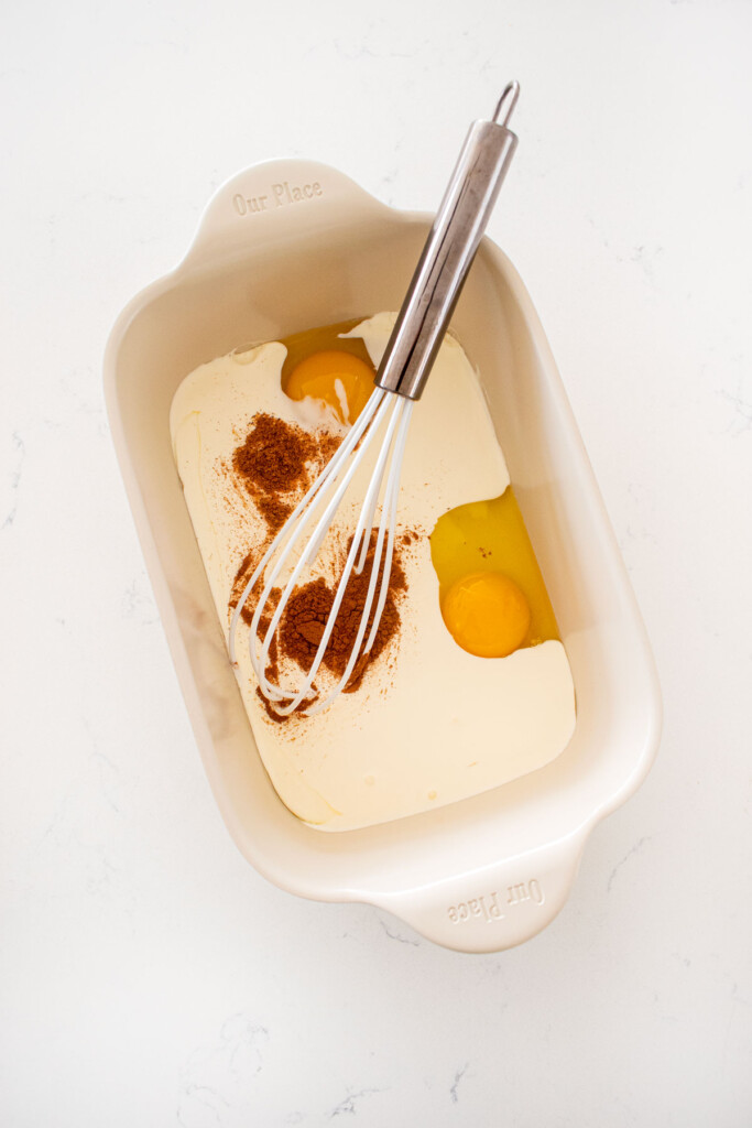 milk, eggs and spices in a shallow baking dish with a whisk on a marble counter.