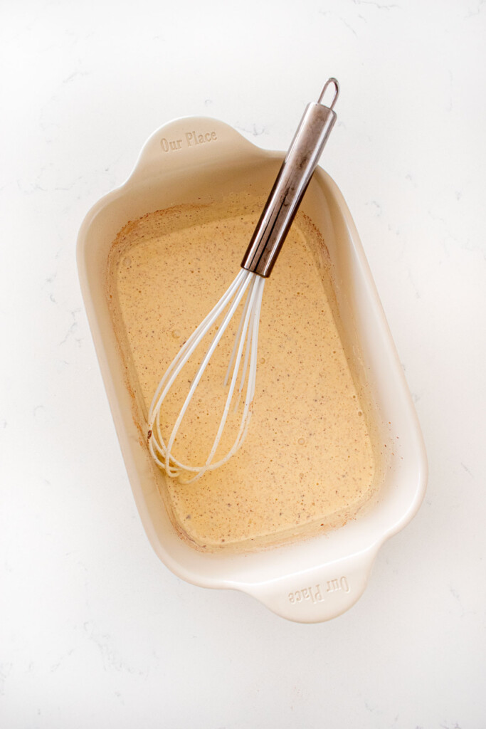 french toast custard mixture whisked together in a shallow baking dish on a white marble counter.