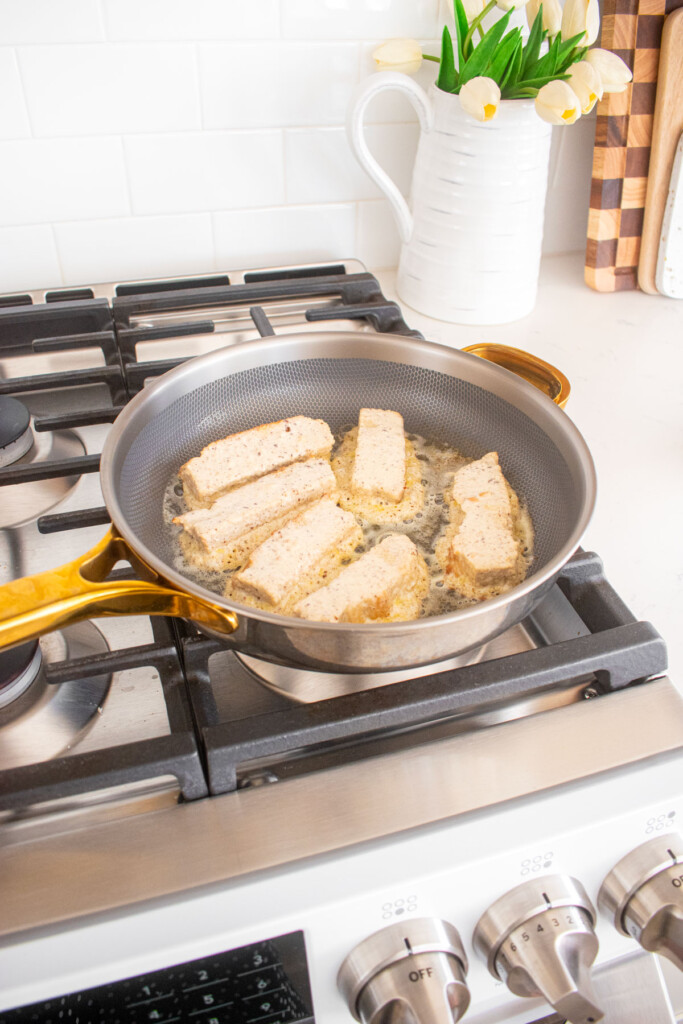 large skillet with french toast sticks being cooked on the stovetop.