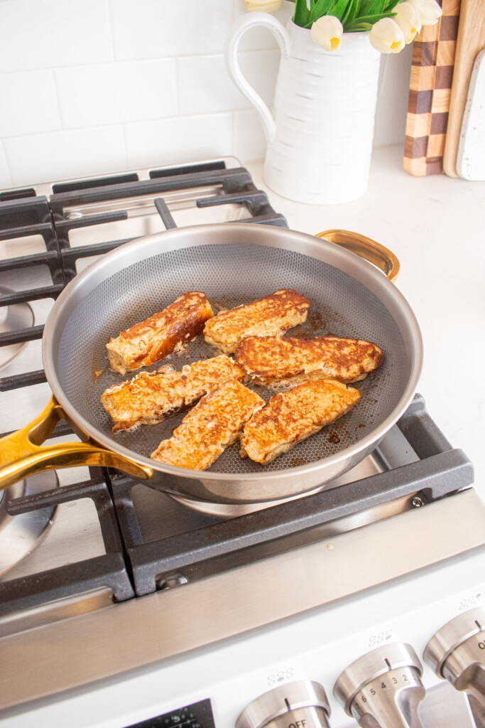 large skillet with french toast sticks being cooked on the stovetop.