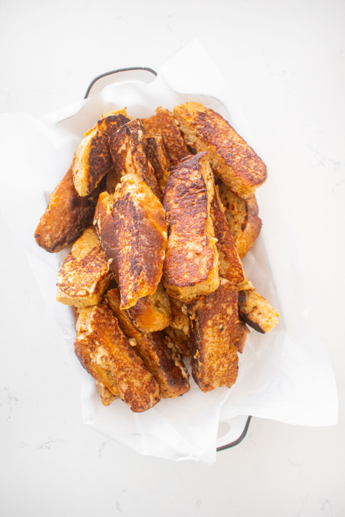 sourdough french toast sticks in a serving platter on a white marble counter.