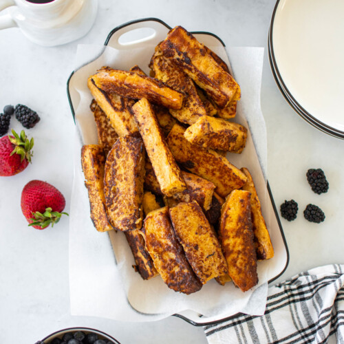 sourdough french toast sticks in on a white serving platter with fresh fruit and maple syrup.