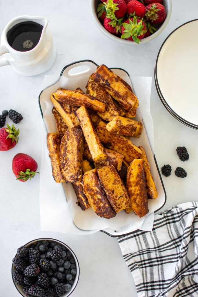 sourdough french toast sticks in on a white serving platter with fresh fruit and maple syrup.