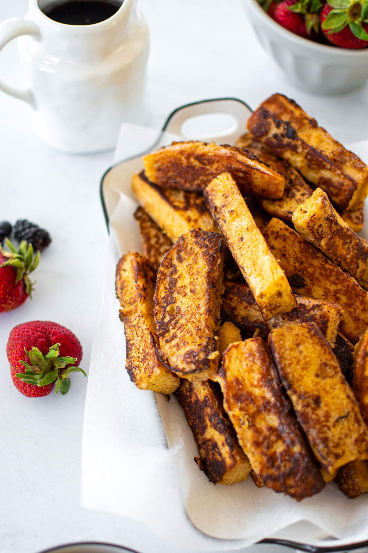 sourdough french toast sticks in on a white serving platter with fresh fruit and maple syrup.