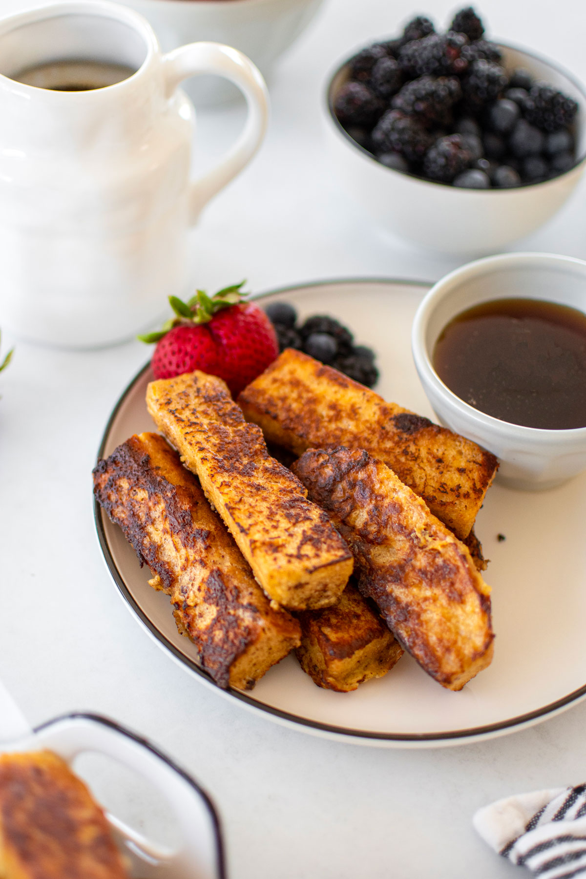 plate of sourdough french toast sticks with maple syrup and fresh fruit on breakfast table.
