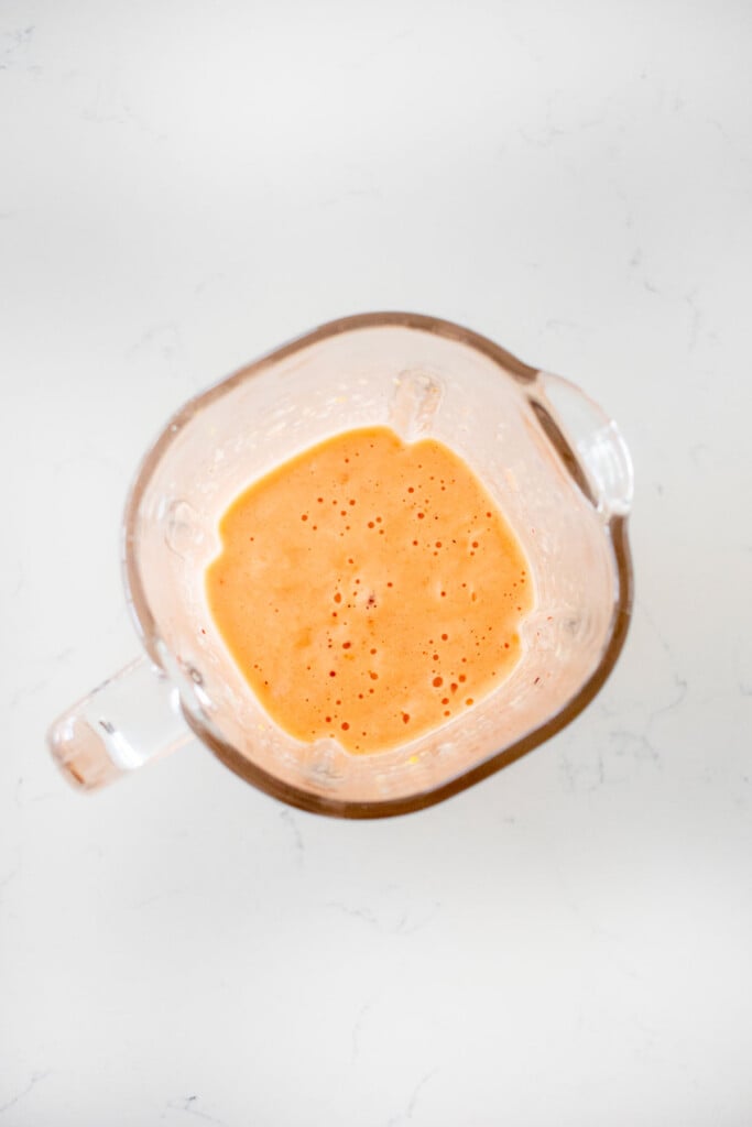 blended strawberry watermelon smoothie in a glass blender on a white marble countertop.