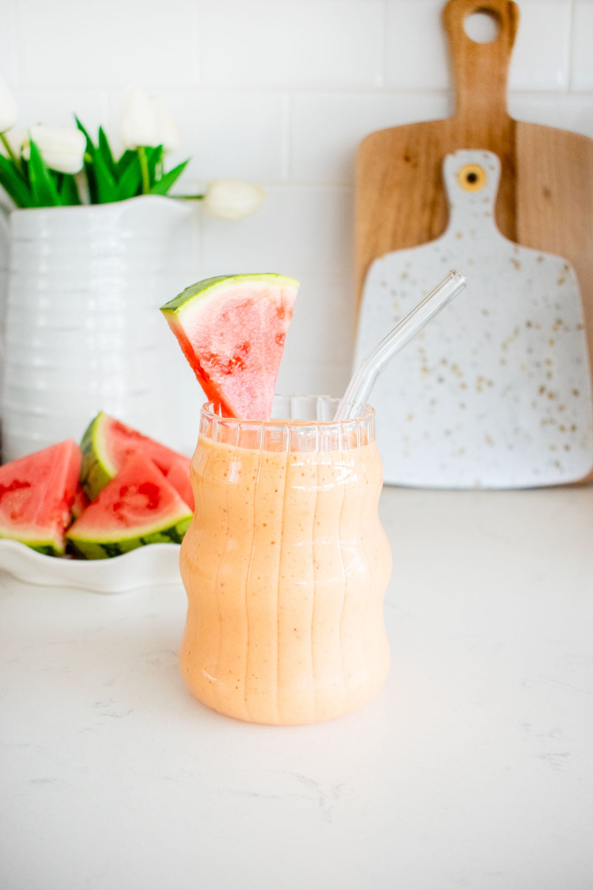 strawberry watermelon smoothie with collagen in a glass with a watermelon slice and straw on kitchen counter.