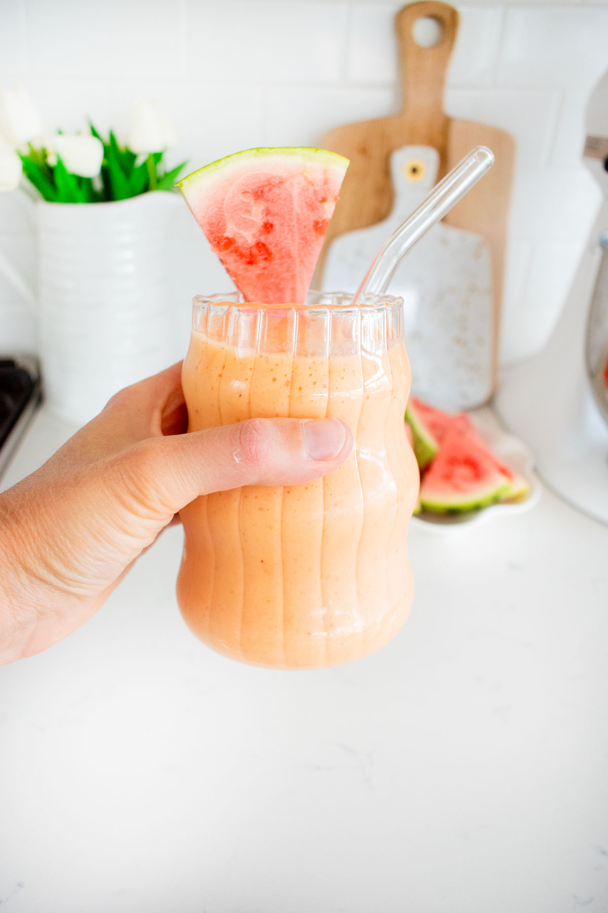 woman holding a glass of strawberry watermelon smoothie with a watermelon slice and straw.