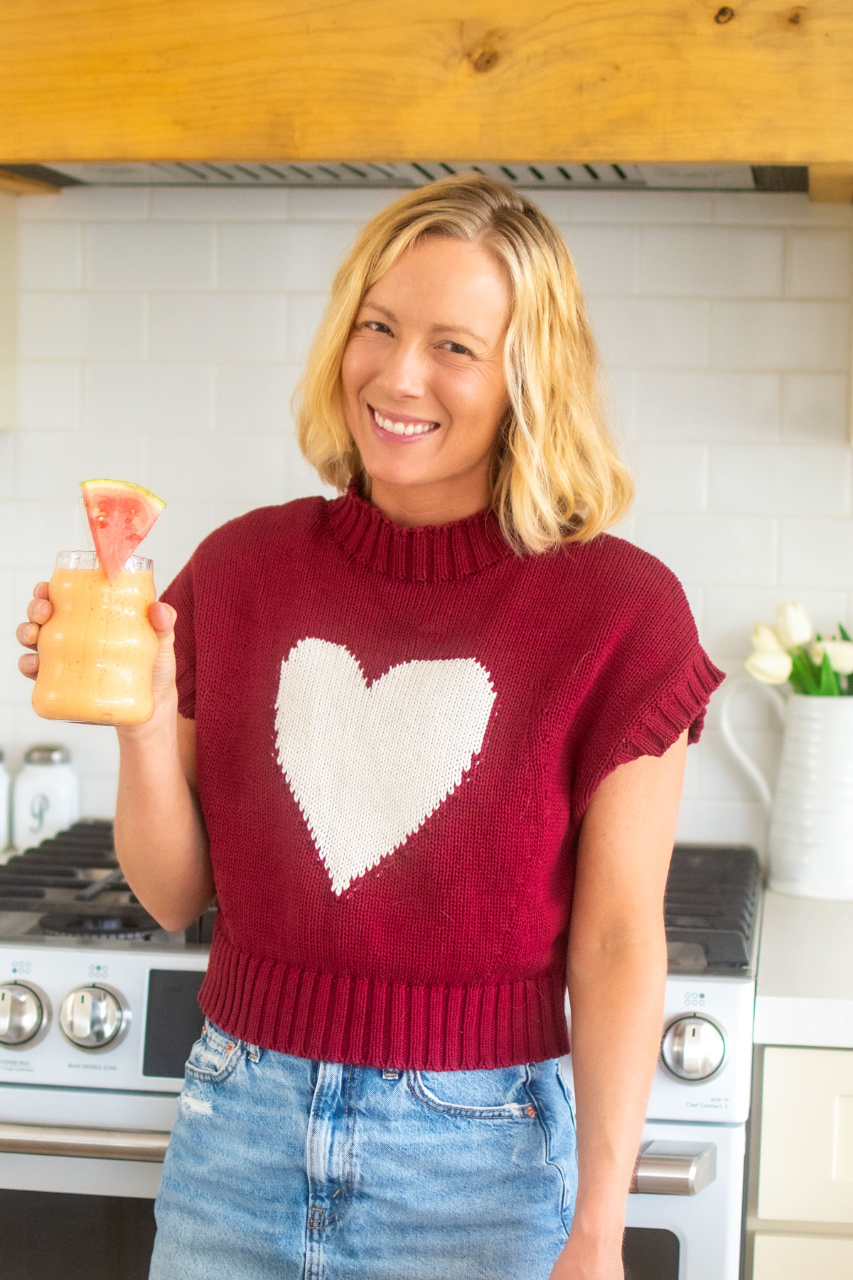 woman holding a strawberry watermelon smoothie with a watermelon slice and straw in the kitchen.