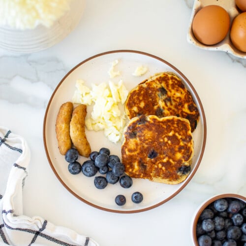 sunday brunch for dogs with pancakes, sausage, eggs and blueberries on a plate on a marble countertop.