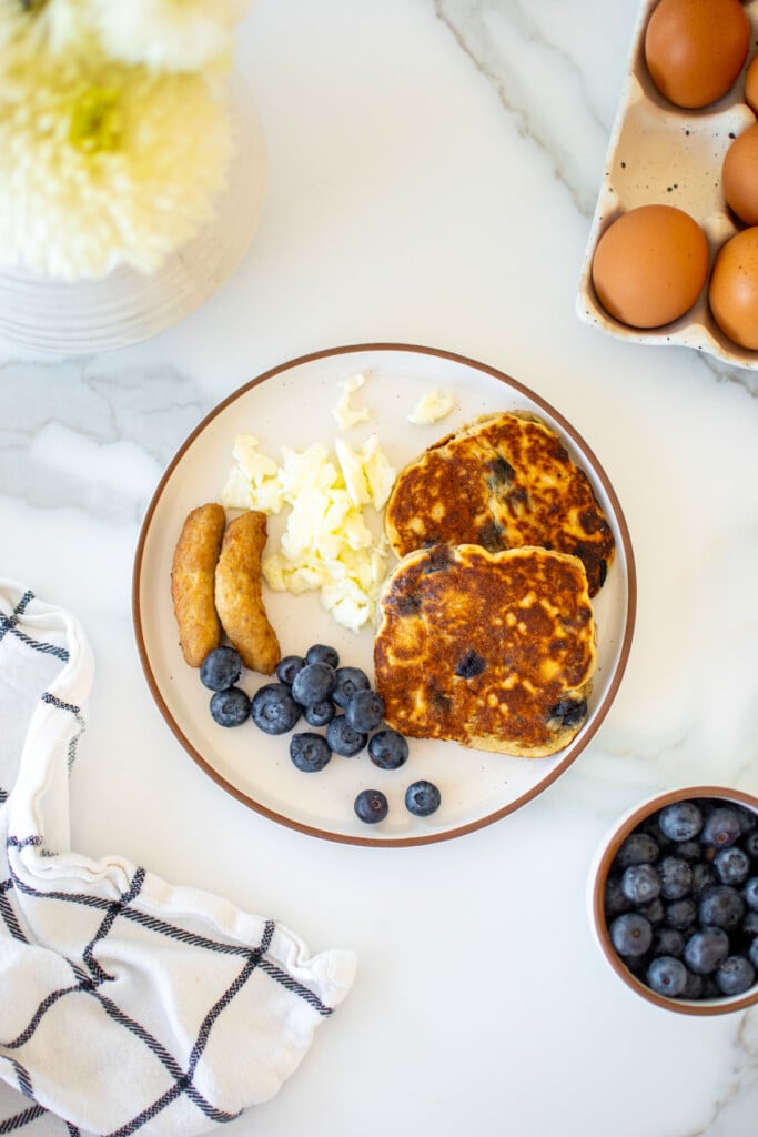 sunday brunch for dogs with pancakes, sausage, eggs and blueberries on a plate on a marble countertop.