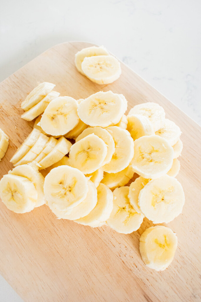 sliced bananas on a wood cutting board on a white marble counter.