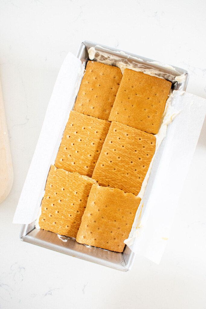 banoffee icebox cake being assembled in a loaf pan on a white marble counter.