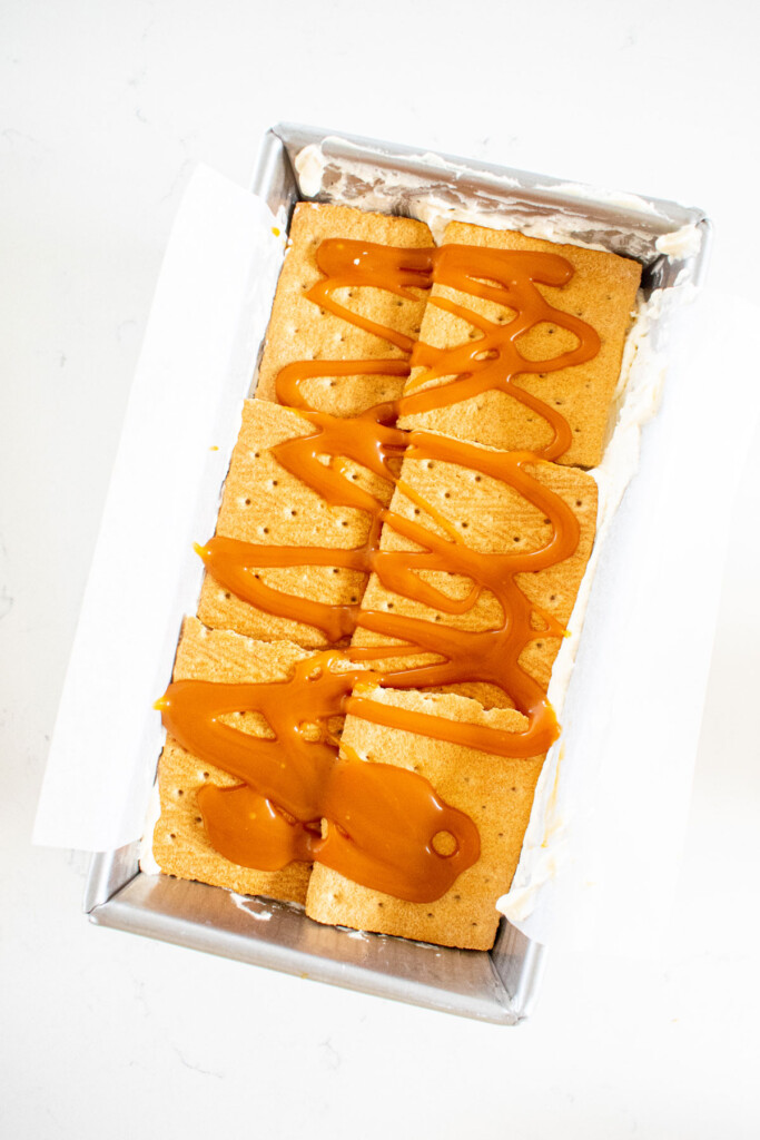 banoffee icebox cake being assembled in a loaf pan on a white marble counter.
