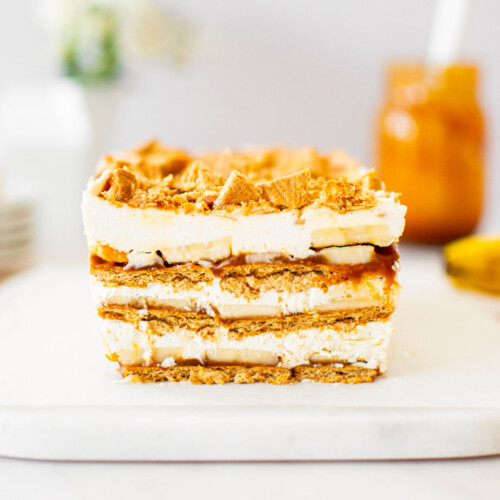 banoffee icebox cake on a white marble serving board on a table with a jar of caramel sauce and flowers.