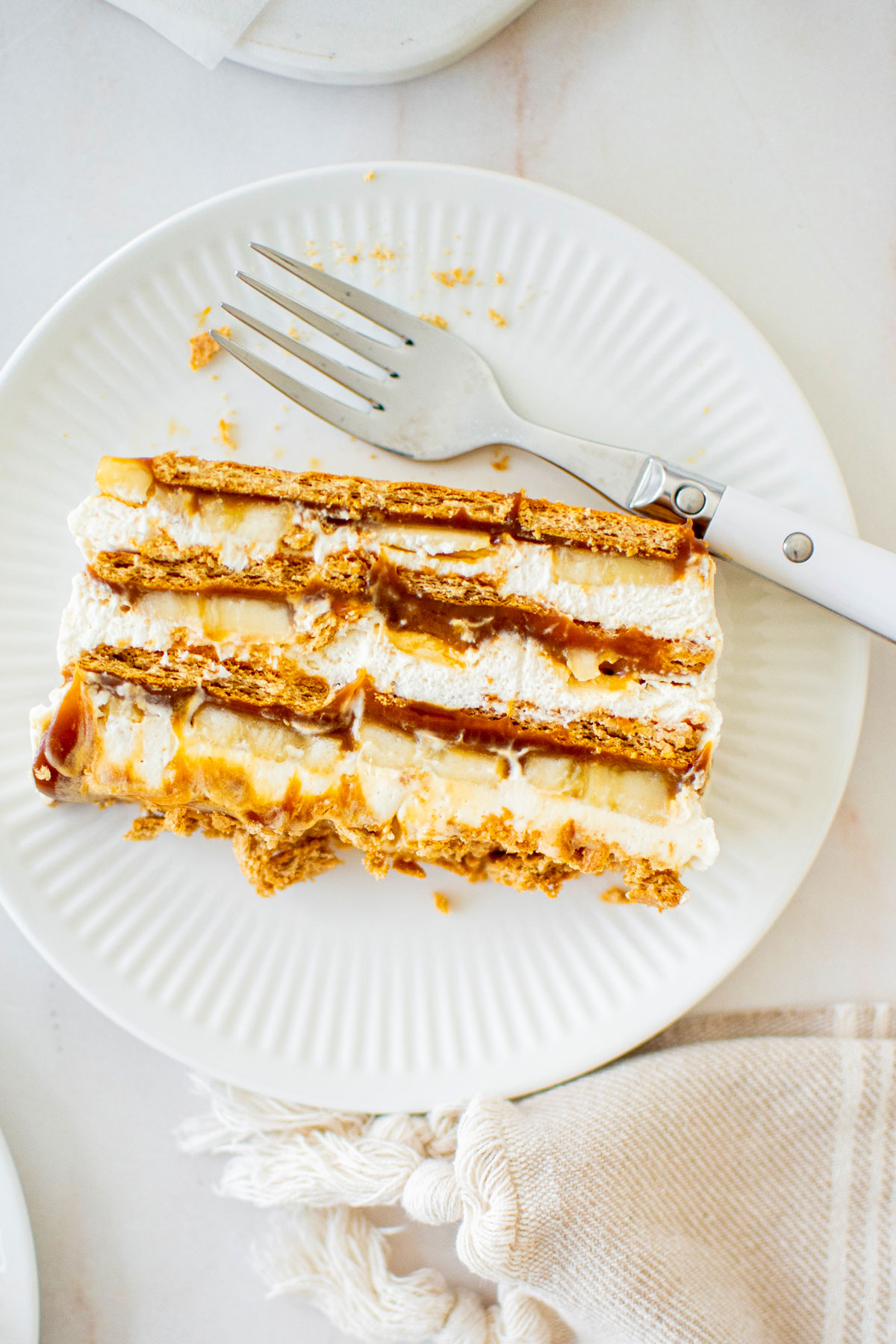slice of banofee icebox cake on a white plate on a marble table.