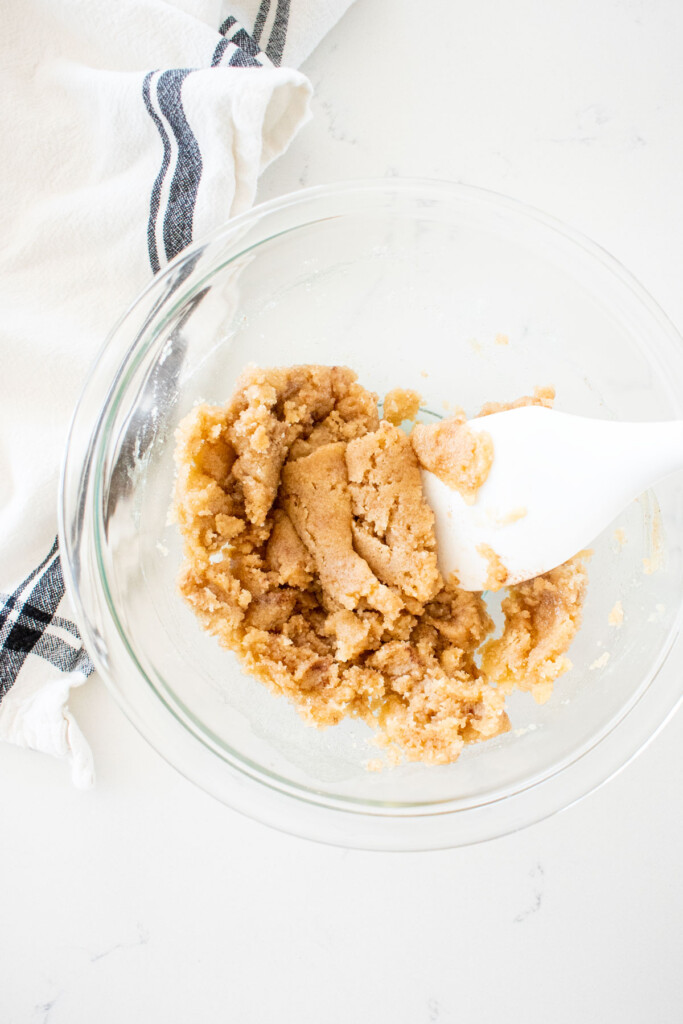 crumble topping mixed together in a glass mixing bowl with a spatula on a marble counter.