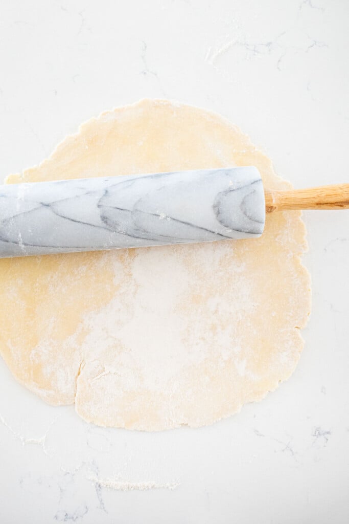 pie dough rolled out on a marble counter with a marble rolling pin.