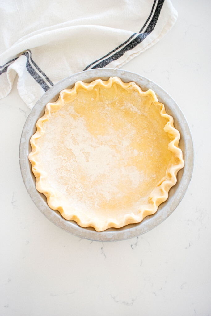 fluted pie crust in an aluminum pie pan on a marble counter.