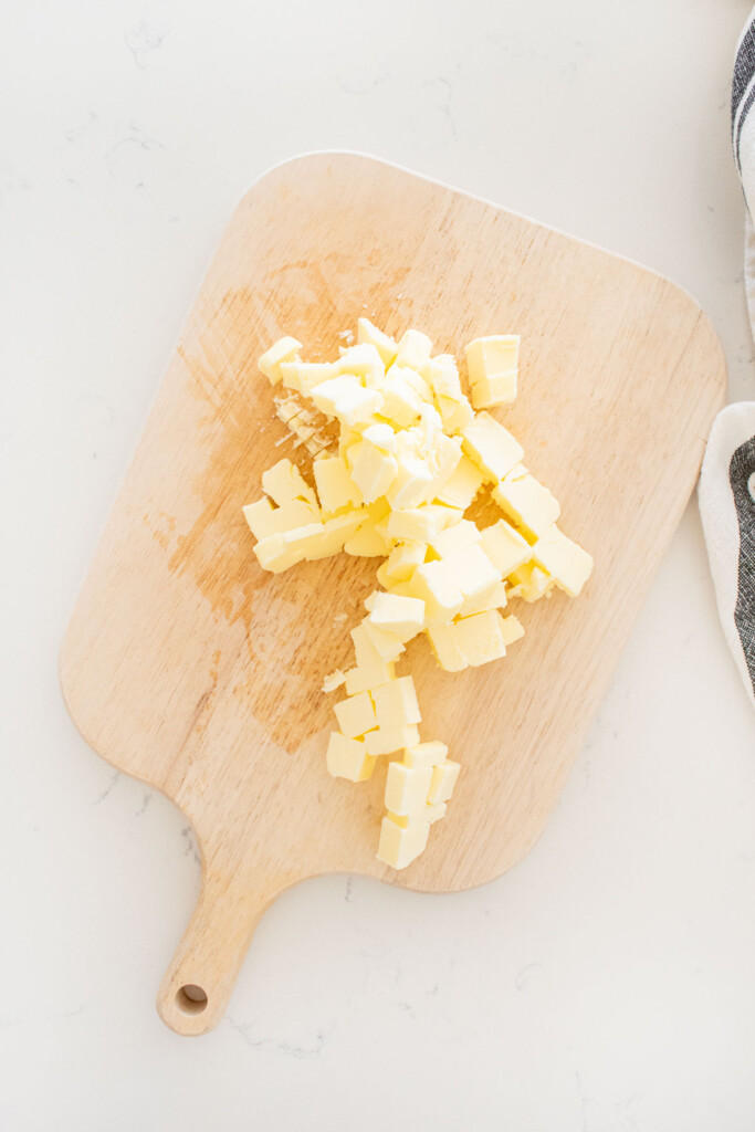 chopped butter on a wood cutting board on a marble counter.