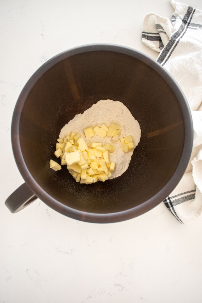 flour with chopped cold butter in a wood mixing bowl on a marble counter.
