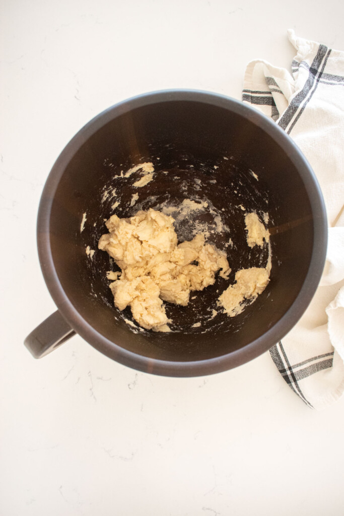 pie dough in a wood mixing bowl on a white marble counter.
