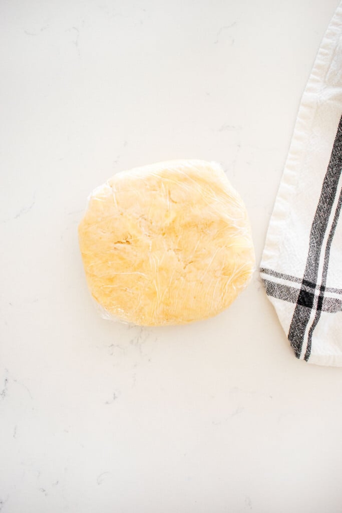 pie dough formed into a disk and wrapped in plastic wrap on a marble counter.