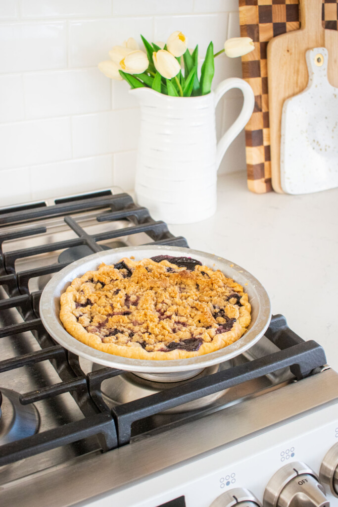 baked blueberry honey crumble pie cooling on top of an oven.