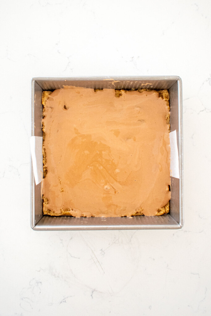 chocolate marshmallow creme spread into baking pan on a white marble counter.