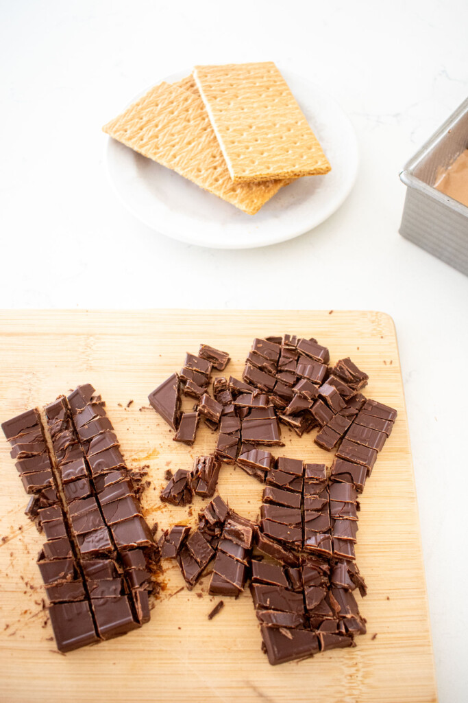 chopped chocolate caramel smore bars on a wood cutting board on a white marble counter.