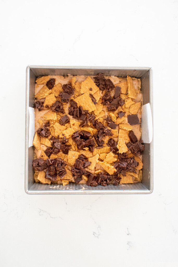 chocolate caramel smore bars in a square baking pan on a white marble counter.