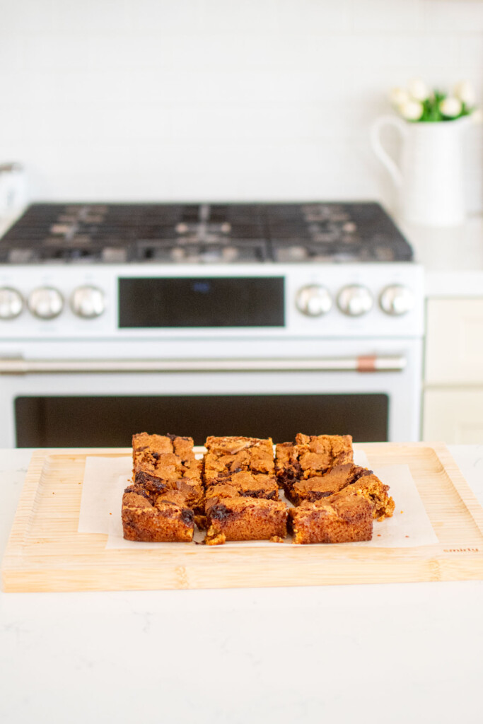 chocolate caramel smore bars cut into squares on a wood cutting board on a white marble counter.