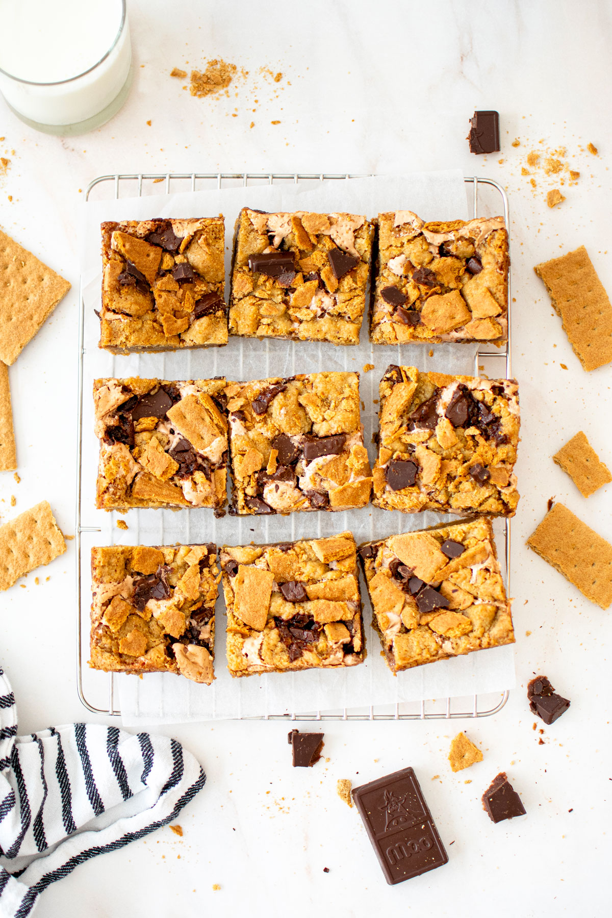 chocolate caramel smore bars cut into 9 squares on a cooling rack on a white marble counter with a glass of milk.