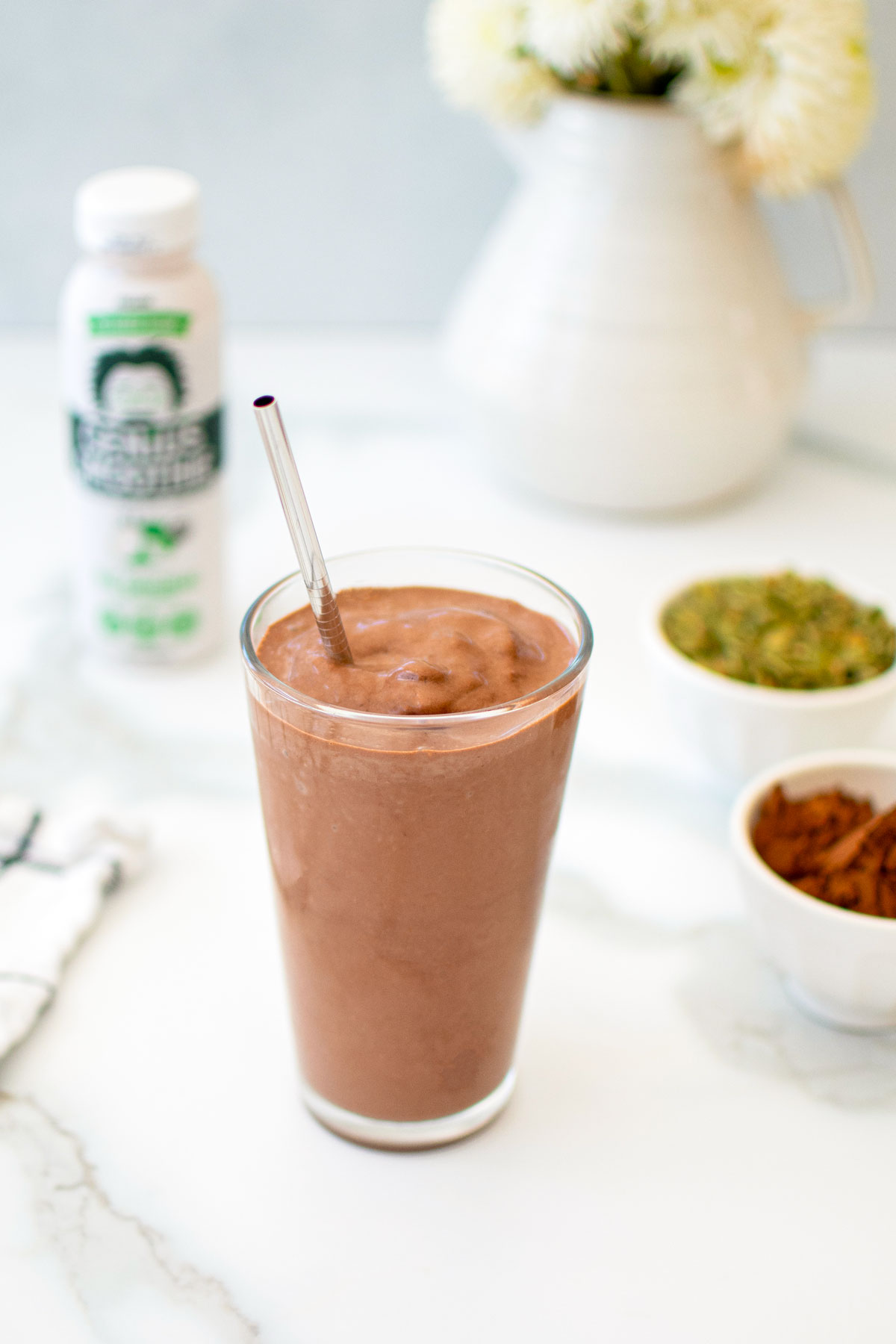 creamy vegan chocolate smoothie with almond butter in a glass with a straw on a white marble counter.