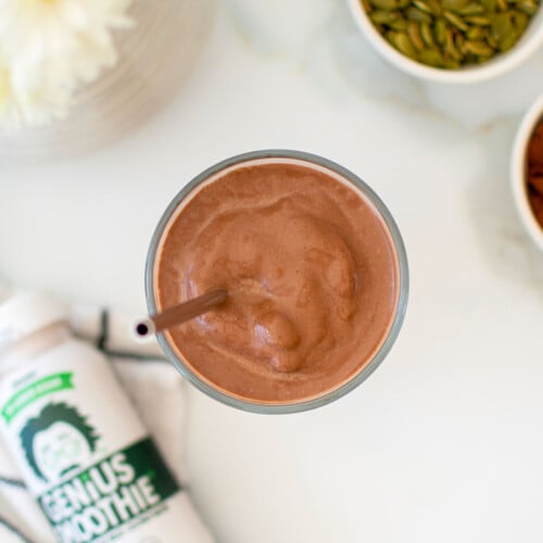 creamy vegan chocolate smoothie with almond butter in a glass with a straw on a white marble counter.