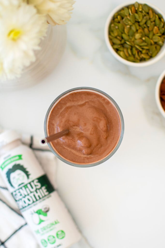 creamy vegan chocolate smoothie with almond butter in a glass with a straw on a white marble counter.