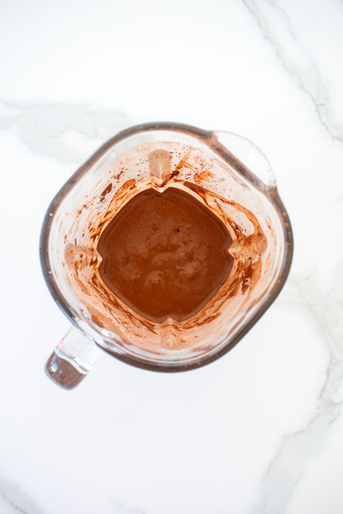 creamy vegan chocolate smoothie with almond butter in a glass blender on a white marble counter.