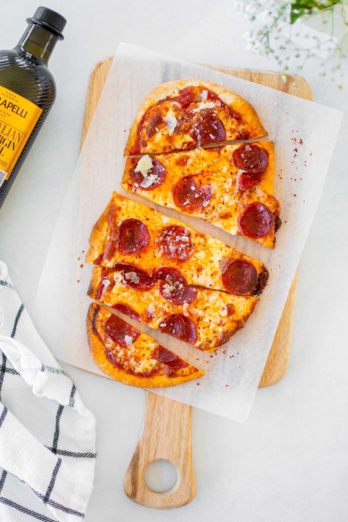 pepperoni flatbread pizza on a wood cutting board on a white table.