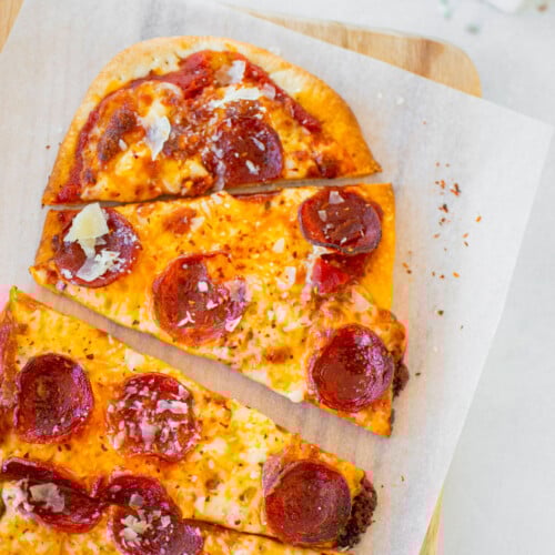 pepperoni flatbread pizza on a wood cutting board on a white table.
