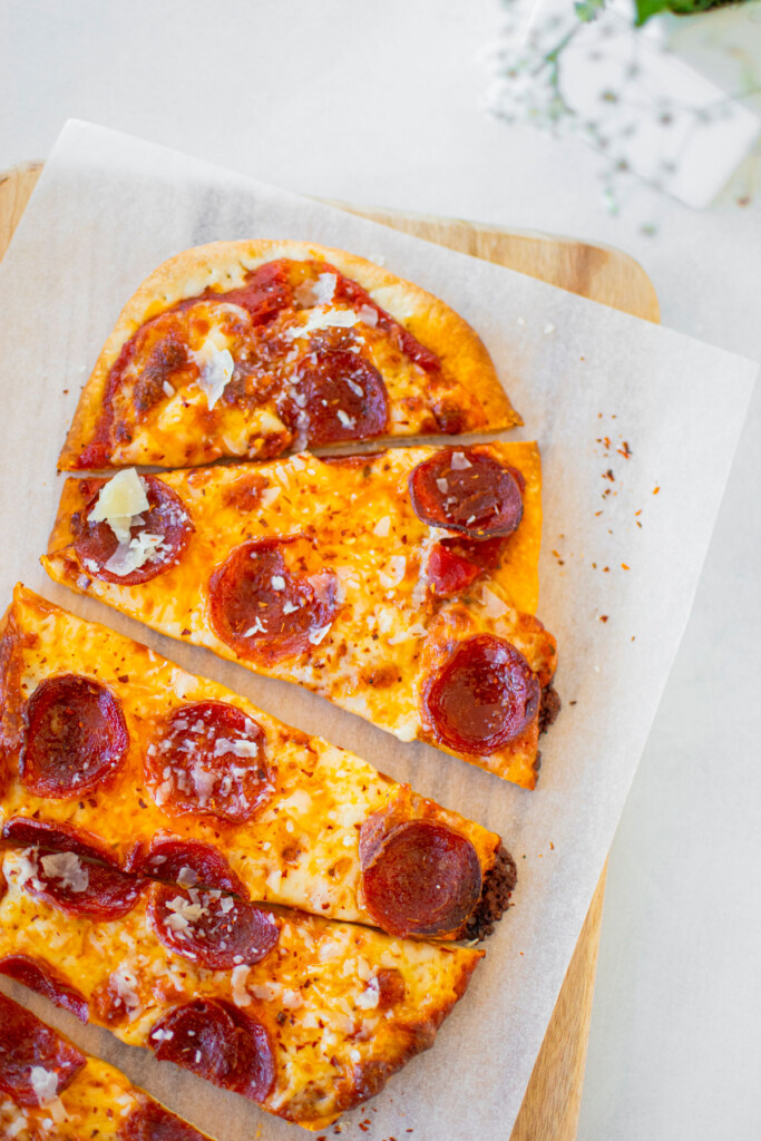 pepperoni flatbread pizza on a wood cutting board on a white table.