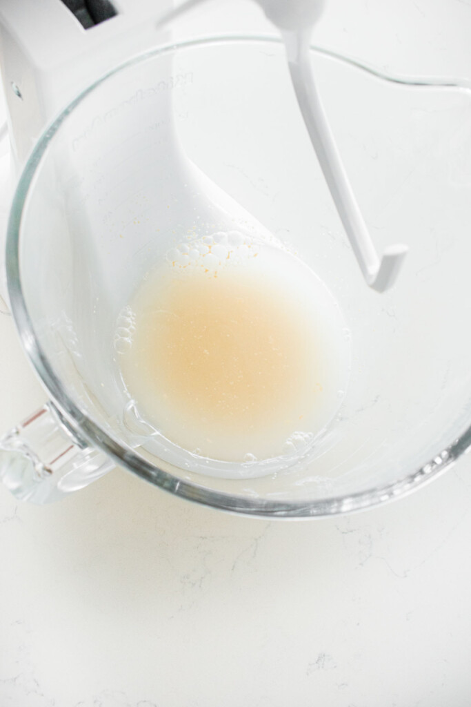yeast and water in a glass stand mixing bowl on a white marble counter.