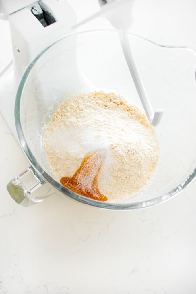 ingredients for homemade sesame bagels in a glass stand mixing bowl on a white marble counter.