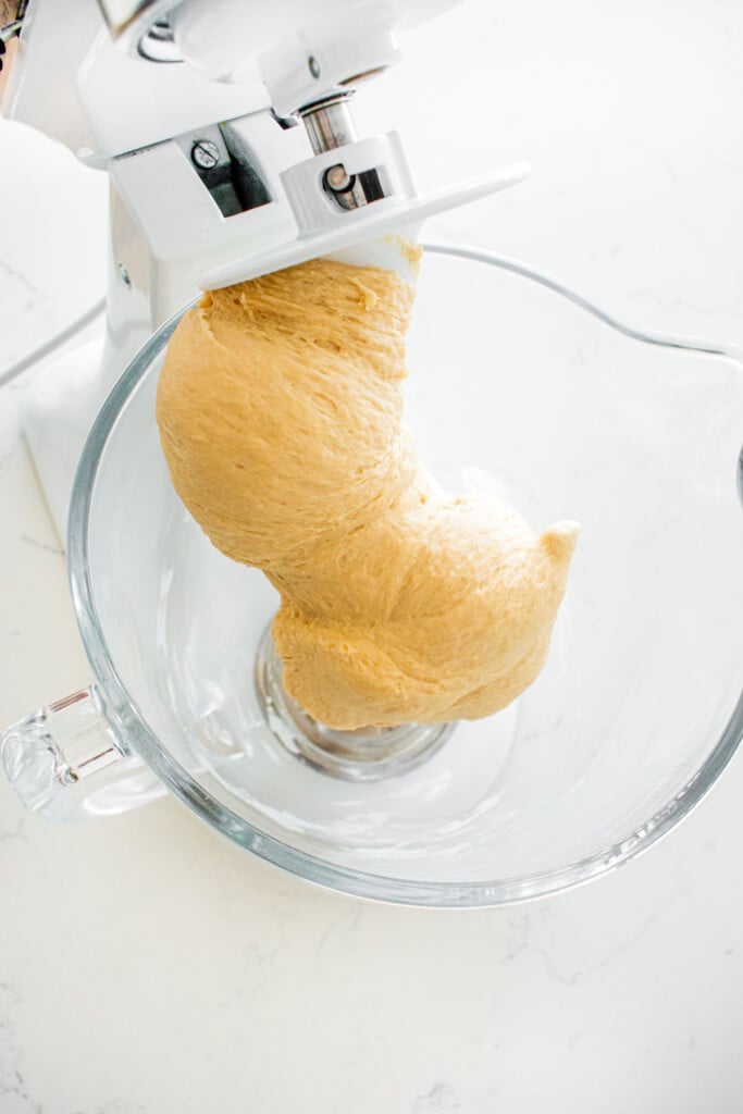 smooth homemade sesame bagel dough in a glass stand mixing bowl on a dough hook.