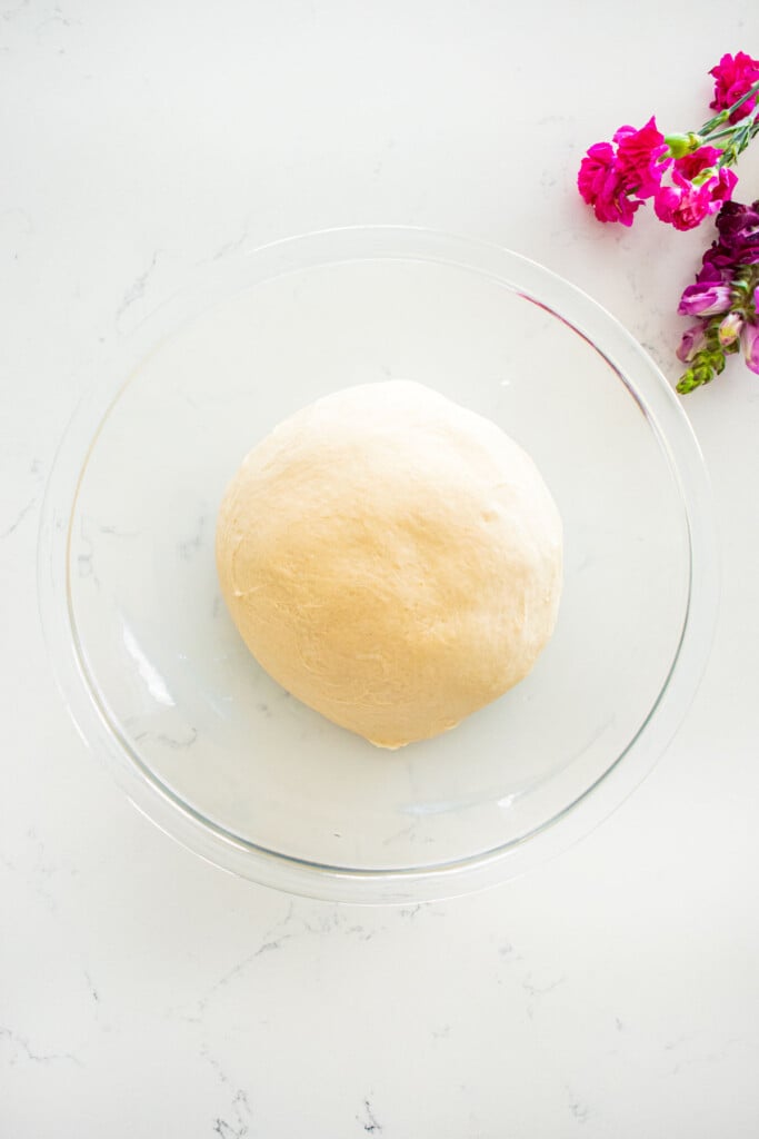 homemade sesame bagel dough ball in a glass mixing bowl on a white marble counter.