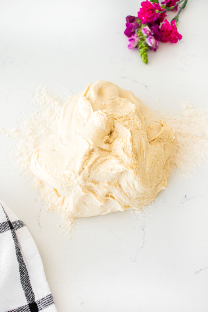homemade sesame bagel dough on a white marble counter with a little flour.