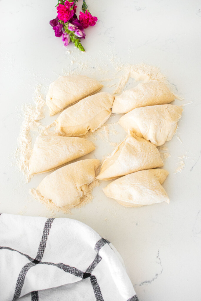 homemade sesame bagel dough divided into 8 pieces on a white marble counter.