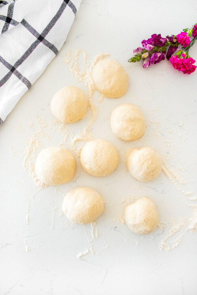 homemade sesame bagel dough divided into 8 pieces and formed into balls on a white marble counter.