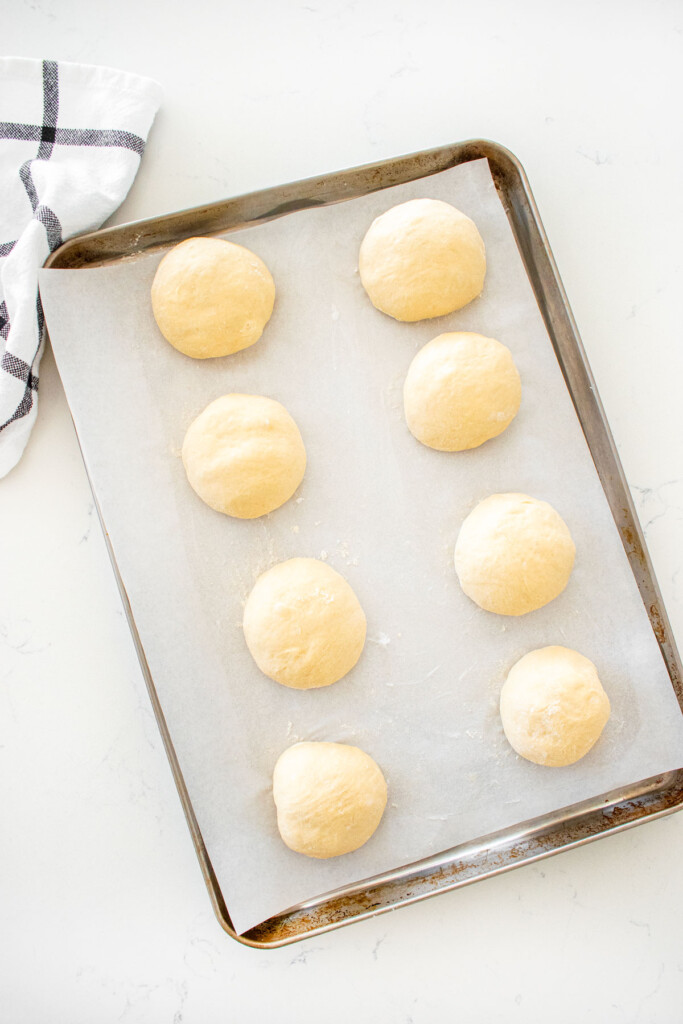 baking sheet with balls of homemade sesame bagel dough on a white marble counter.